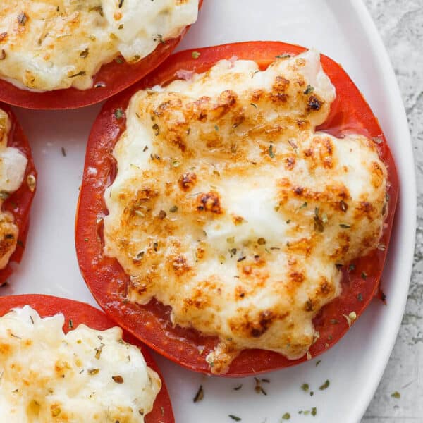 Plate of broiled tomatoes with a parmesan mayo mixture on top.