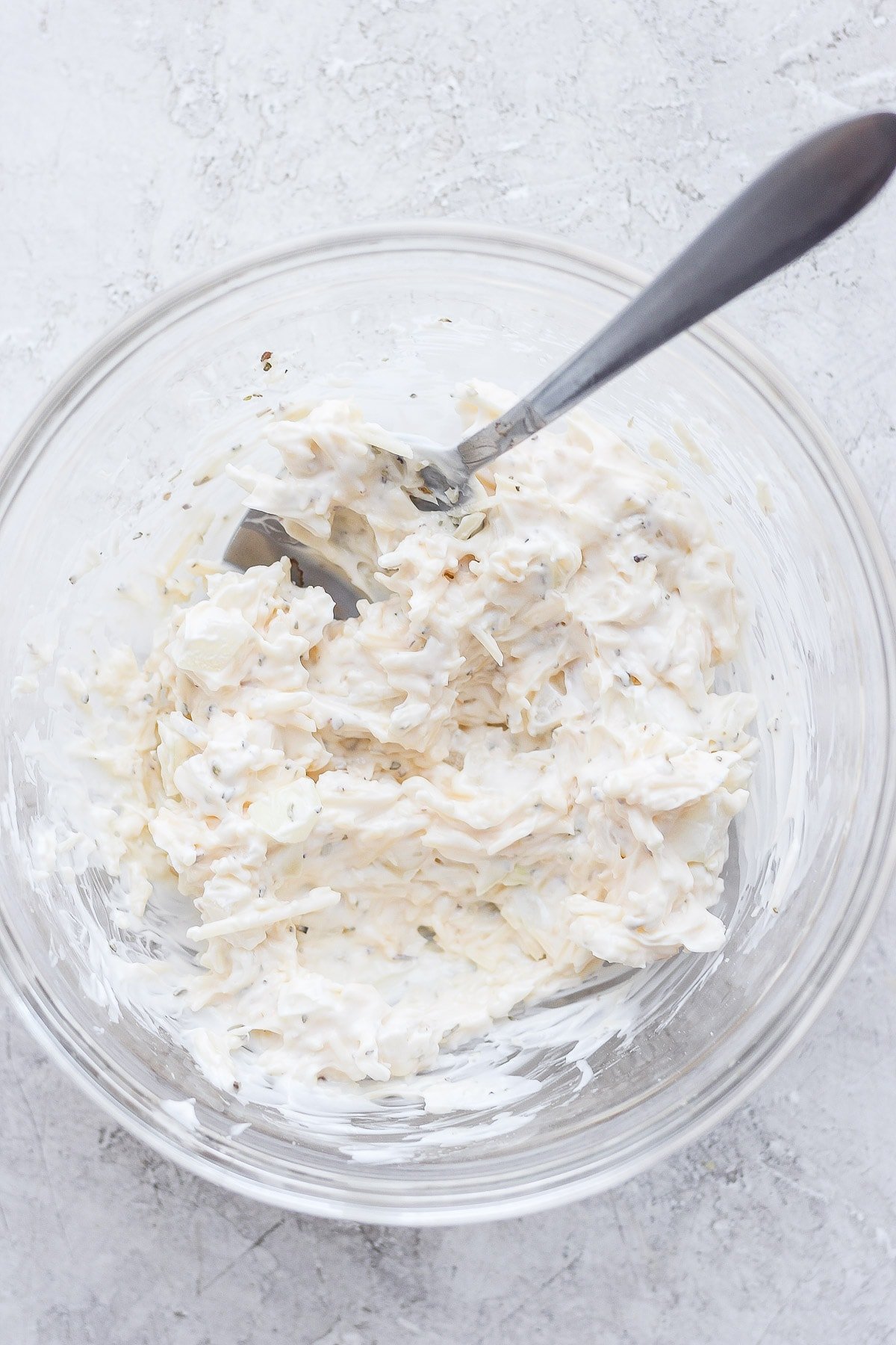 Glass bowl with mayo, parmesan cheese, onion and oregano inside mixed up. 