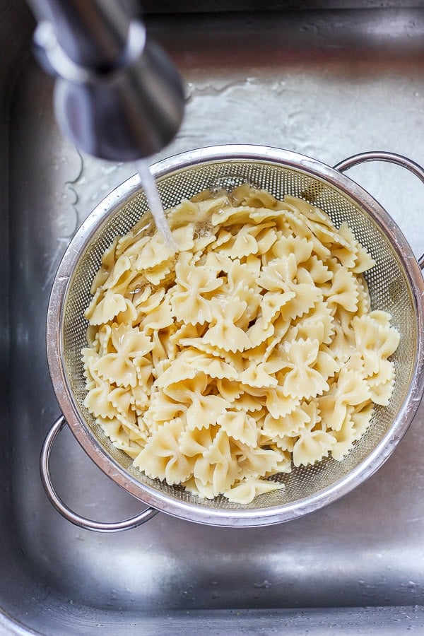 Cooked farfalle pasta in a colander being rinsed with cold water.