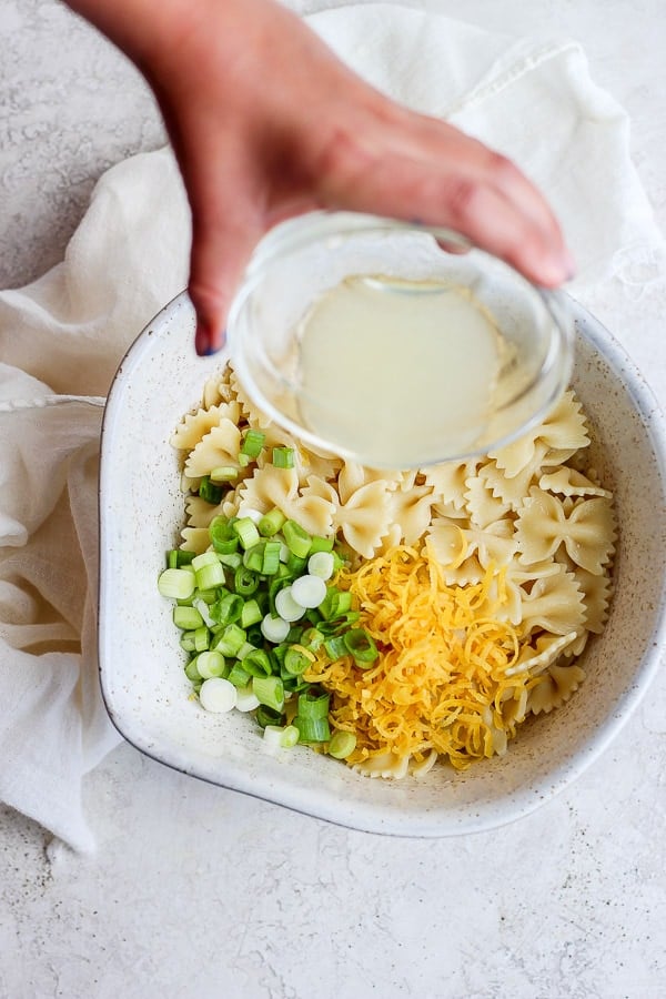 Someone pouring lemon juice into a bowl of pasta, green onions and lemon zest.