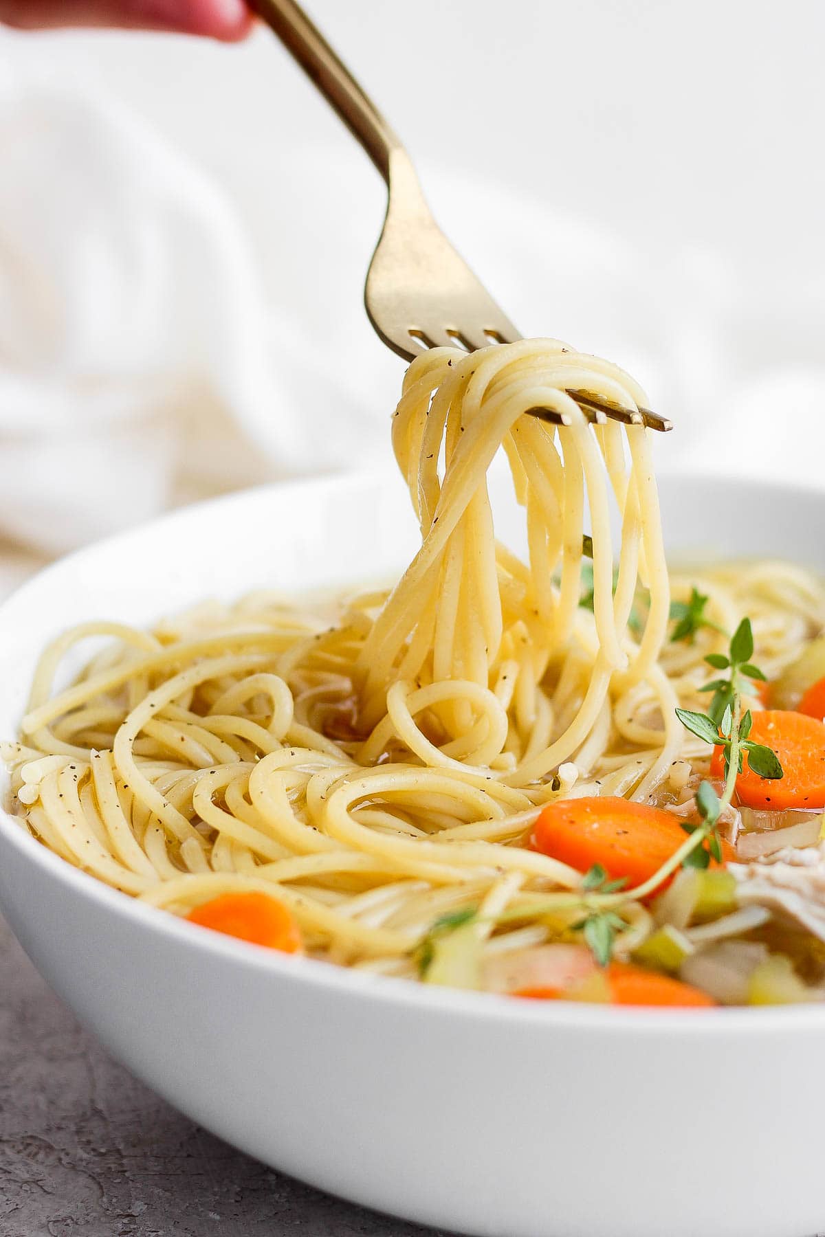 A bowl of slow cooker chicken noodle soup with a fork pulling out some noodles. 