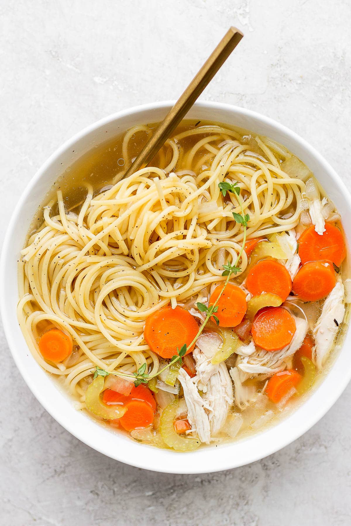 A bowl of slow cooker chicken noodle soup with a spoon sticking out. 