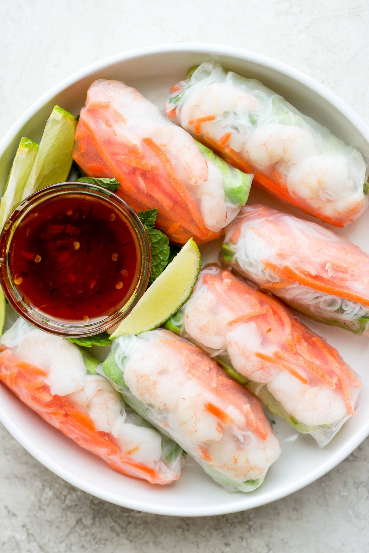 Bowl of shrimp spring rolls with a smaller bowl of dipping sauce and a few lime slices. 