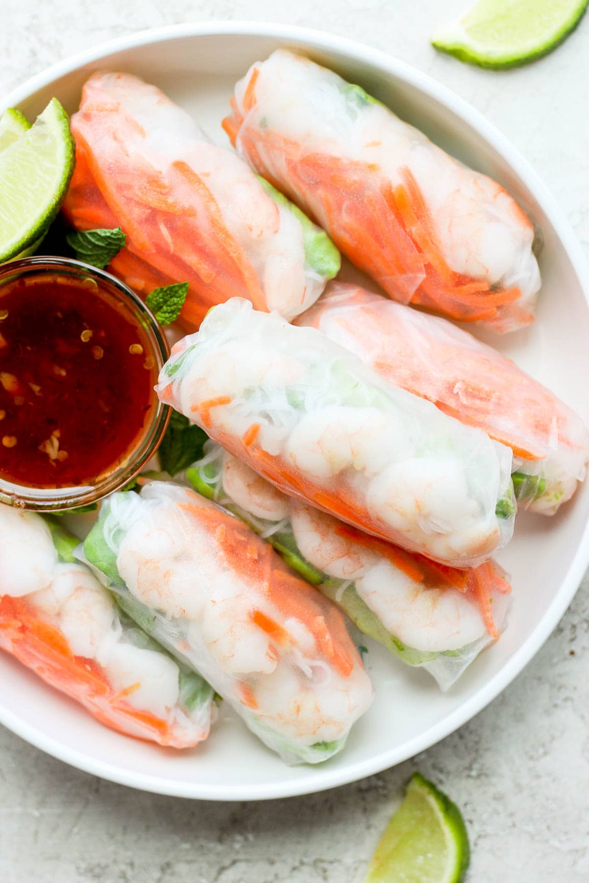 Bowl of shrimp spring rolls with a smaller bowl of dipping sauce and a few lime slices. 