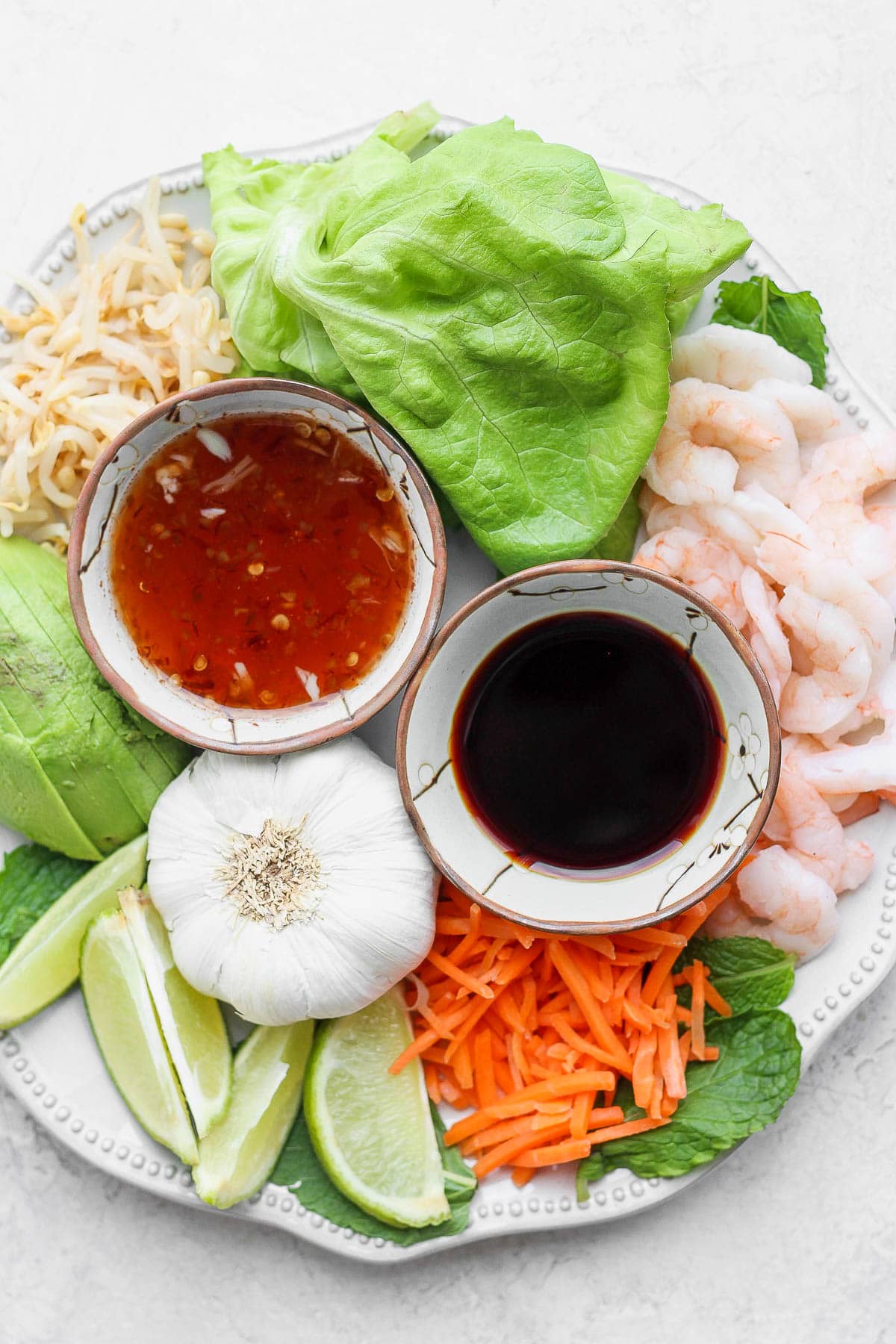 Ingredients for spring rolls on a large plate or platter including lettuce, bean sprouts, avocado, carrots and shrimp. 