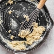 A roux in a cast iron skillet with a whisk sticking out.
