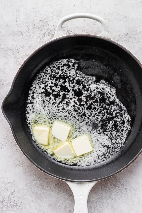 4 tablespoons of butter being melted in a cast iron pan.