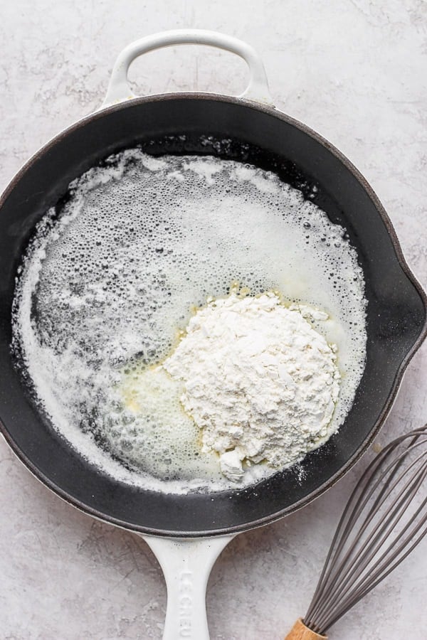 Flour added to a cast iron pan of melted butter and a whisk off to the side.