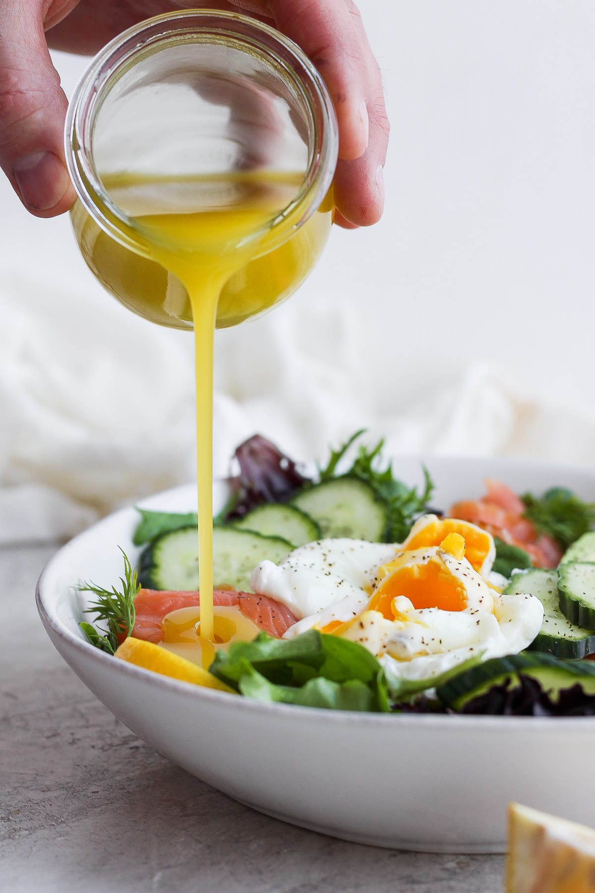 Someone pouring lemon dill vinaigrette into a bowl of salad. 