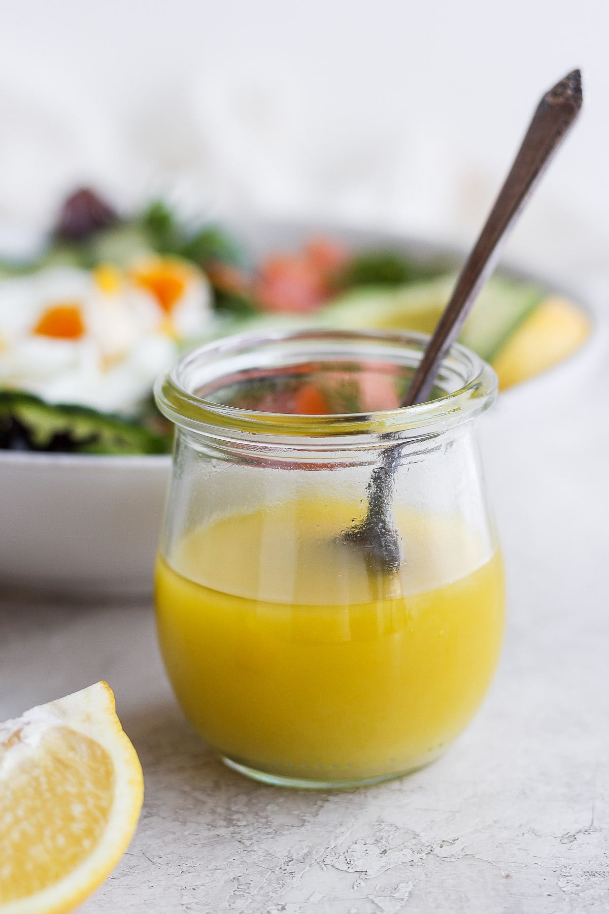 Little jar of lemon dill vinaigrette with a bowl of salad in the background. 