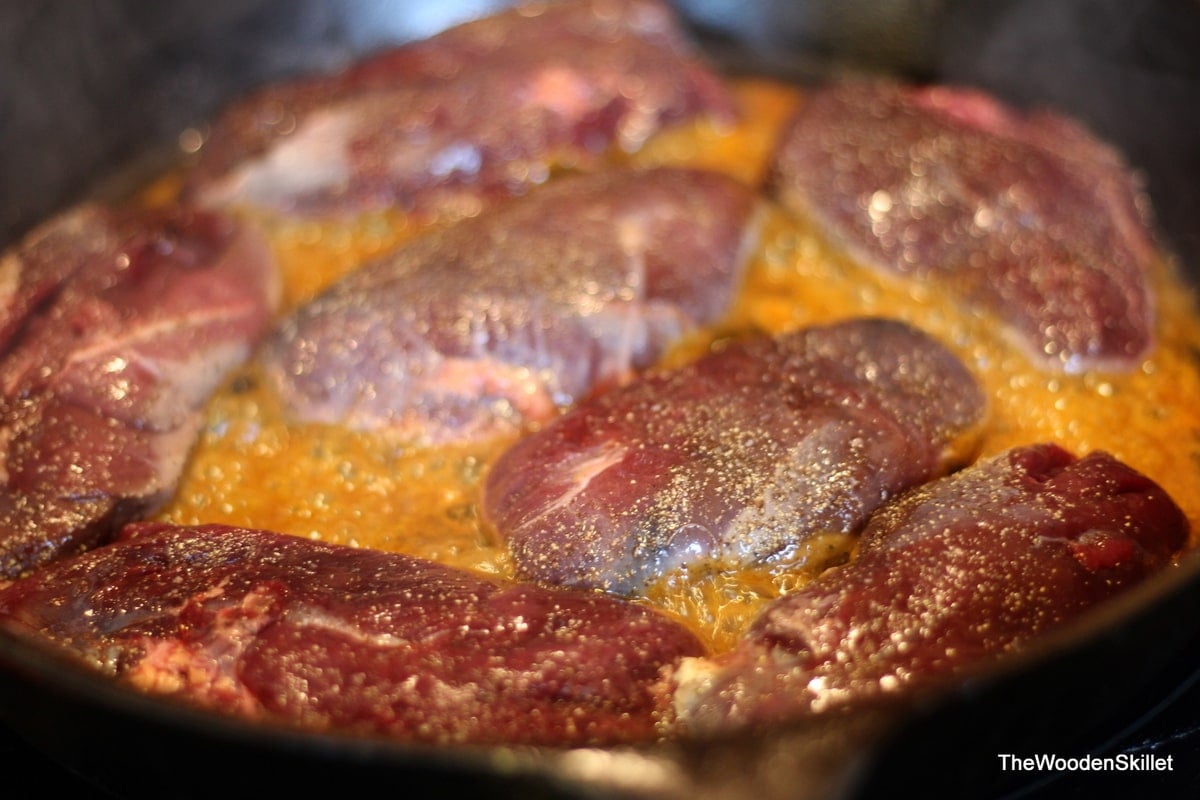 Duck breasts searing in a cast iron skillet with olive oil and a little curry sauce.
