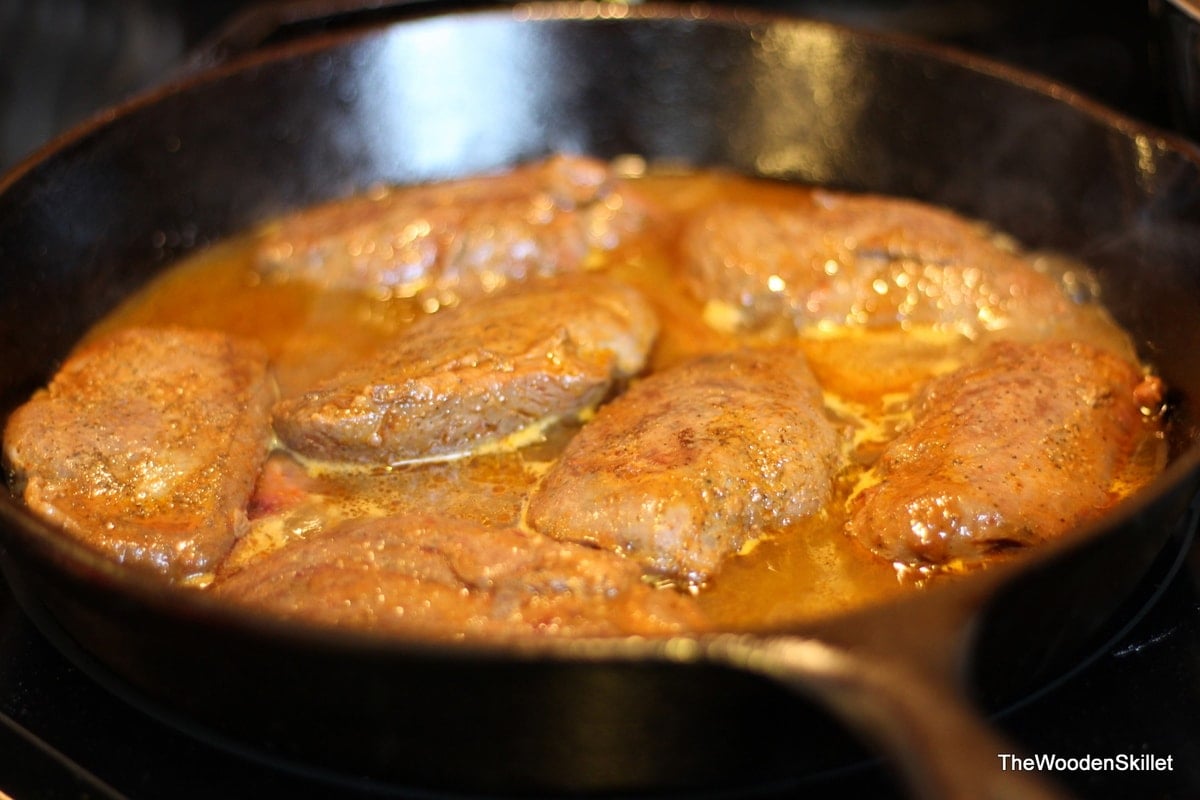 Duck breasts searing in the cast iron skillet after being flipped.