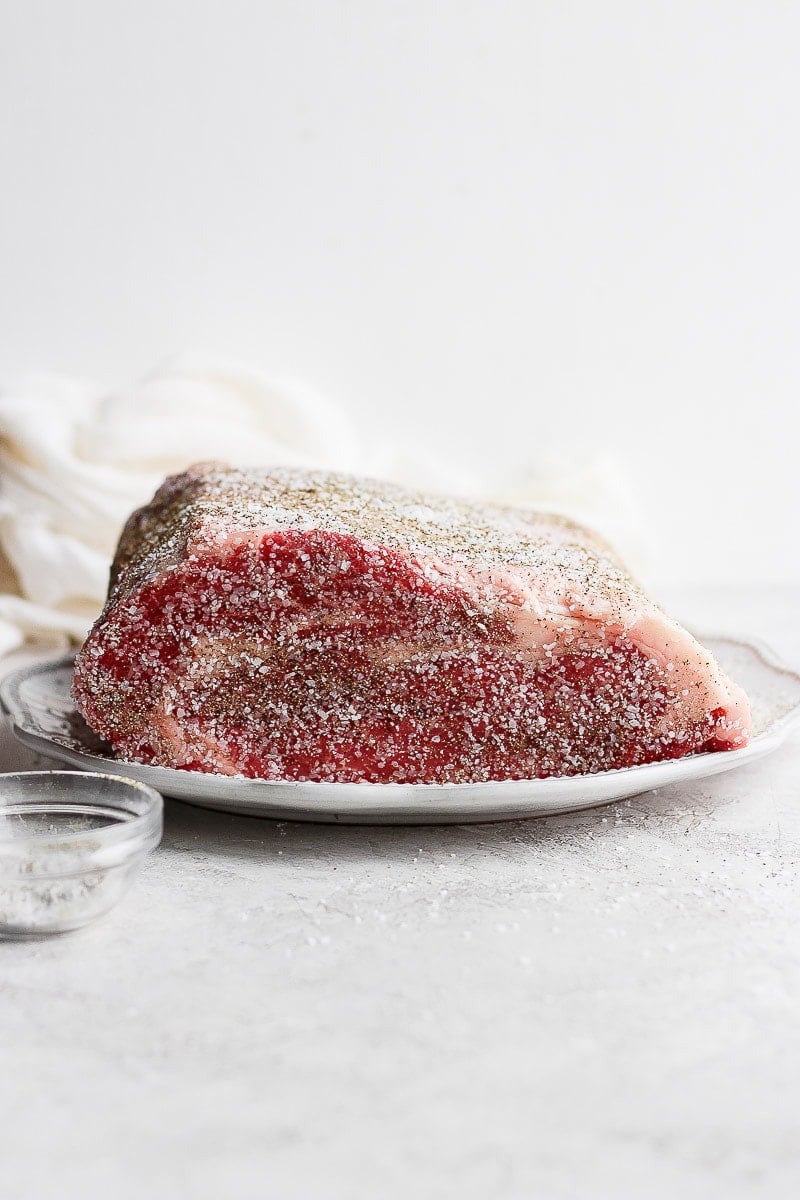 Raw prime rib on a plate with salt and pepper rub. 