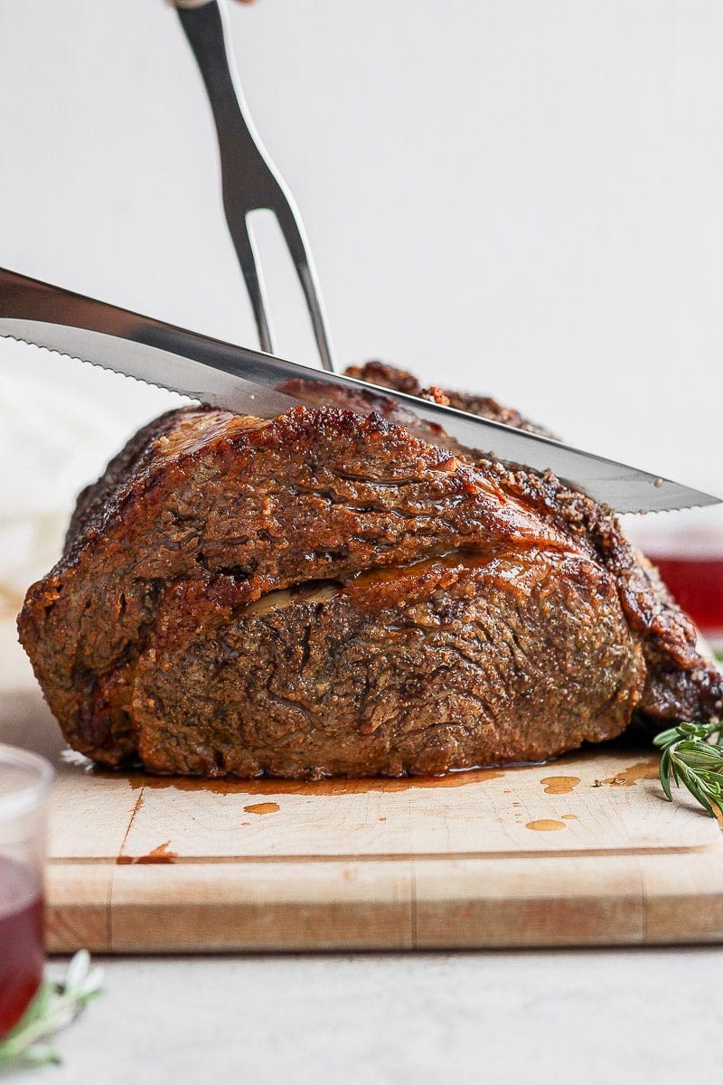 Standing rib roast on a cutting board with a knife cutting into it. 