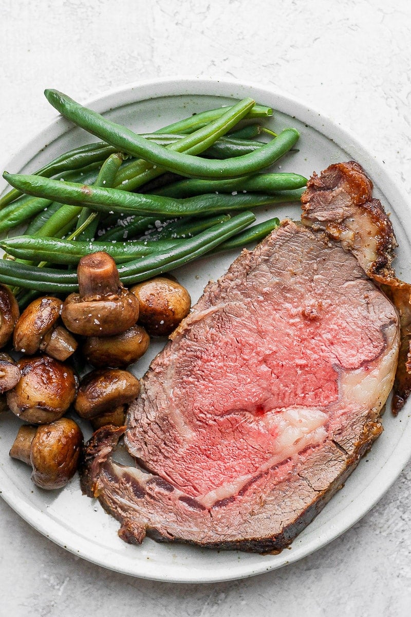 A slice of prime rib on a plate with mushrooms and green beans.