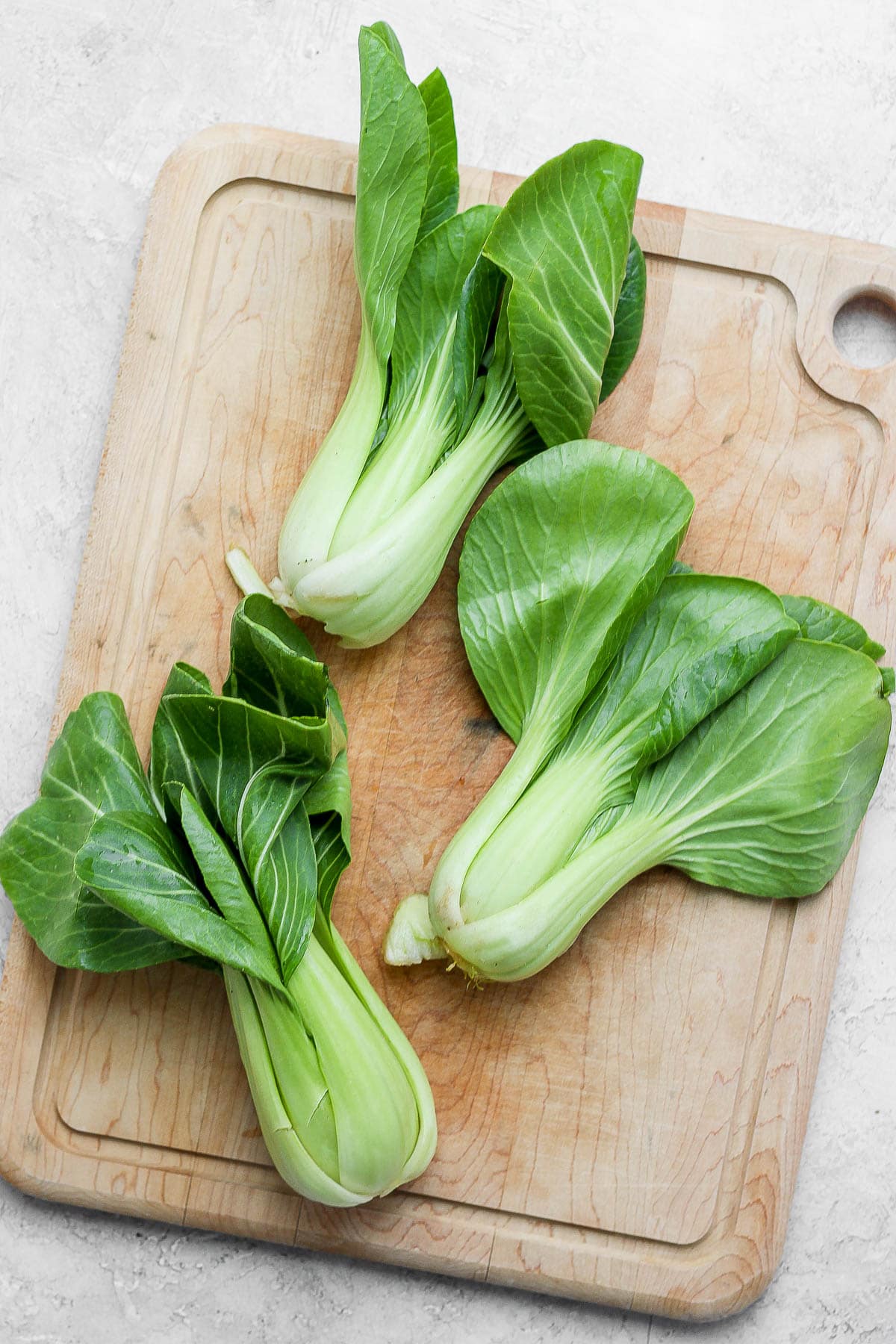 A large wooden cutting board with three baby bok choy on top. 