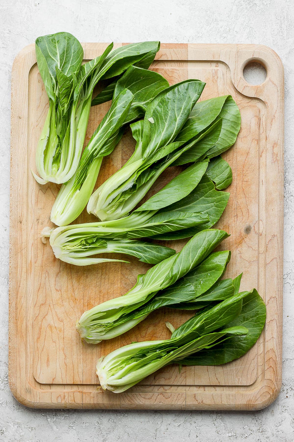 A wooden cutting board filed with baby bok choy all cut in half lengthwise. 