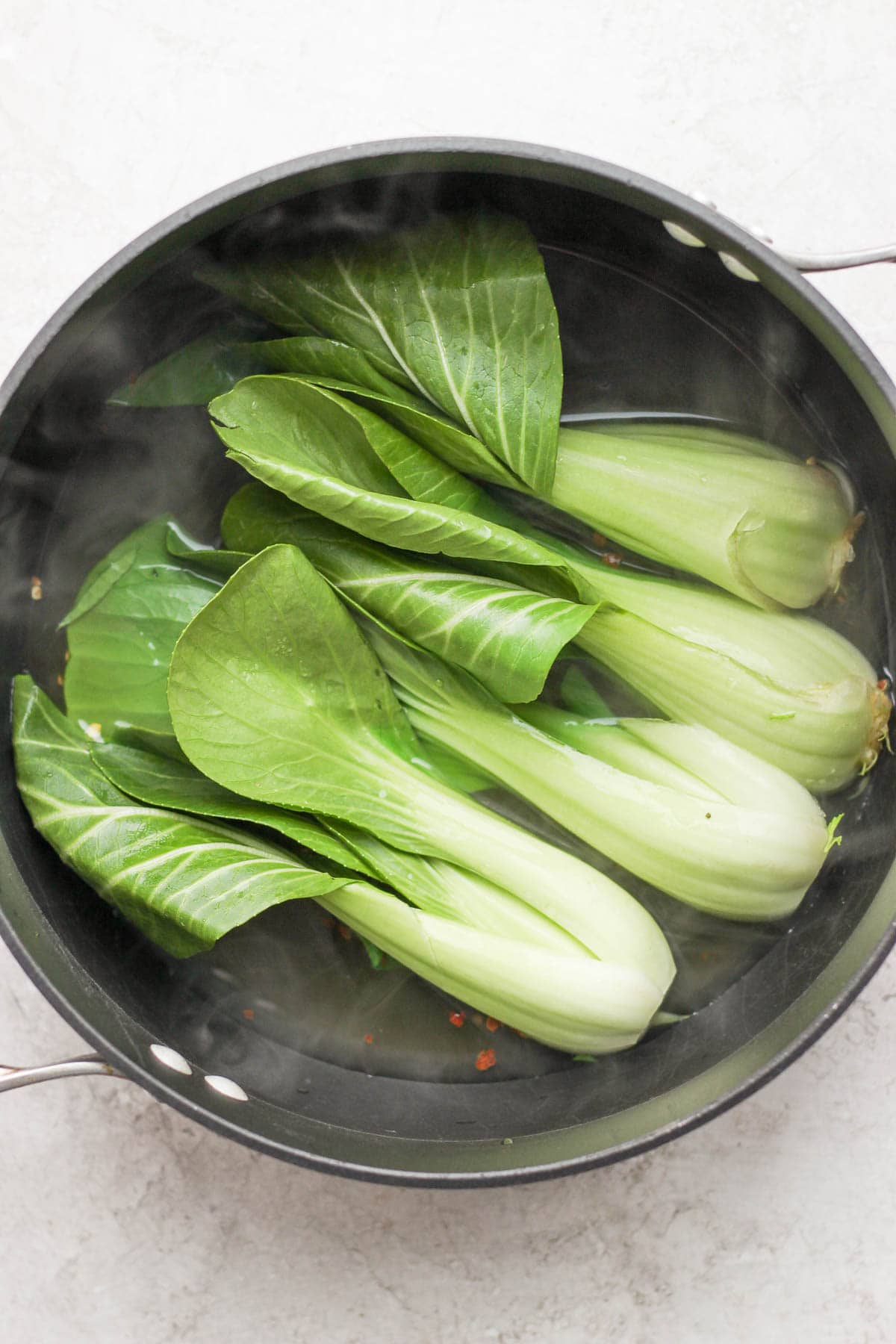 A black dutch oven with 4 halved baby bok choy being braised inside. 