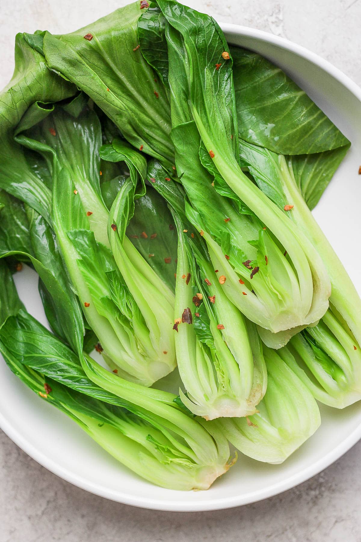 A large white bowl filled with braised bok choy and topped with red pepper flakes.