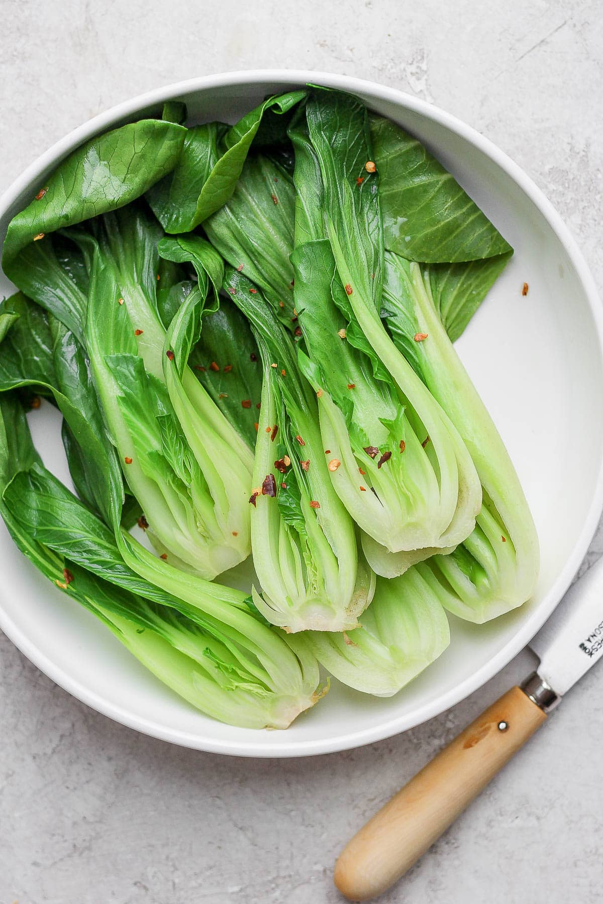 A large white bowl filled with braised bok choy and topped with red pepper flakes. 