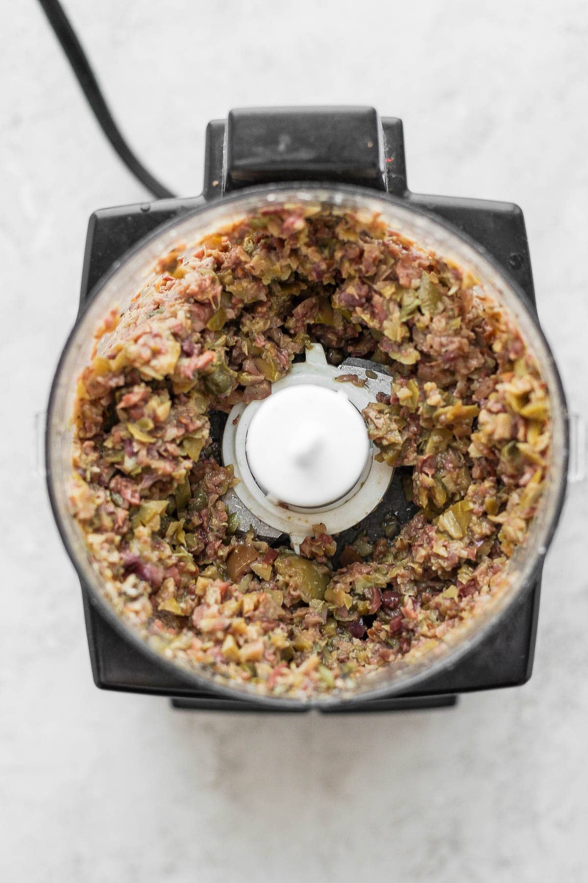 Top shot of a food processor with olive tapenade inside.