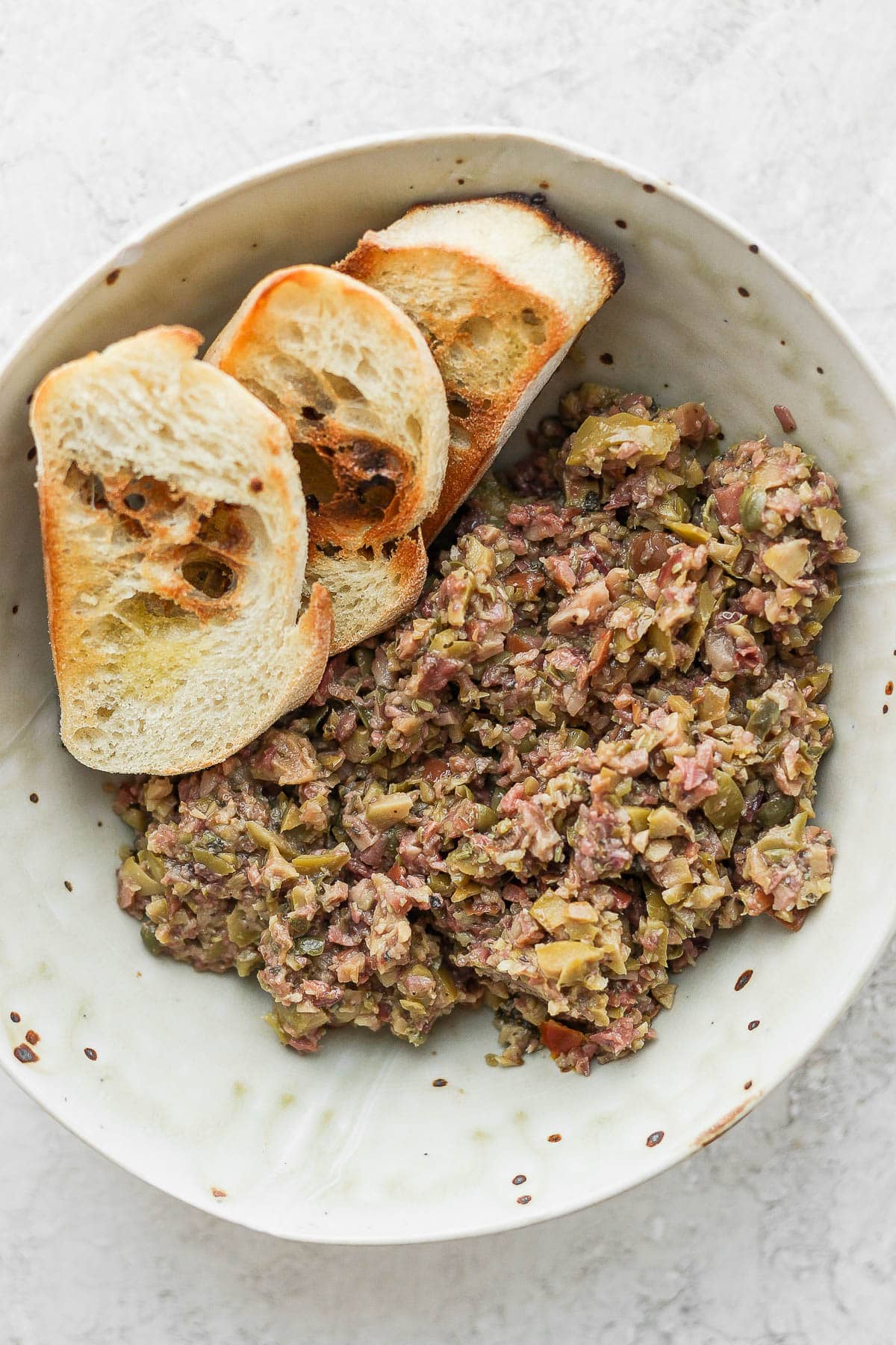 Bowl of olive tapenade with three pieces of baguette. 