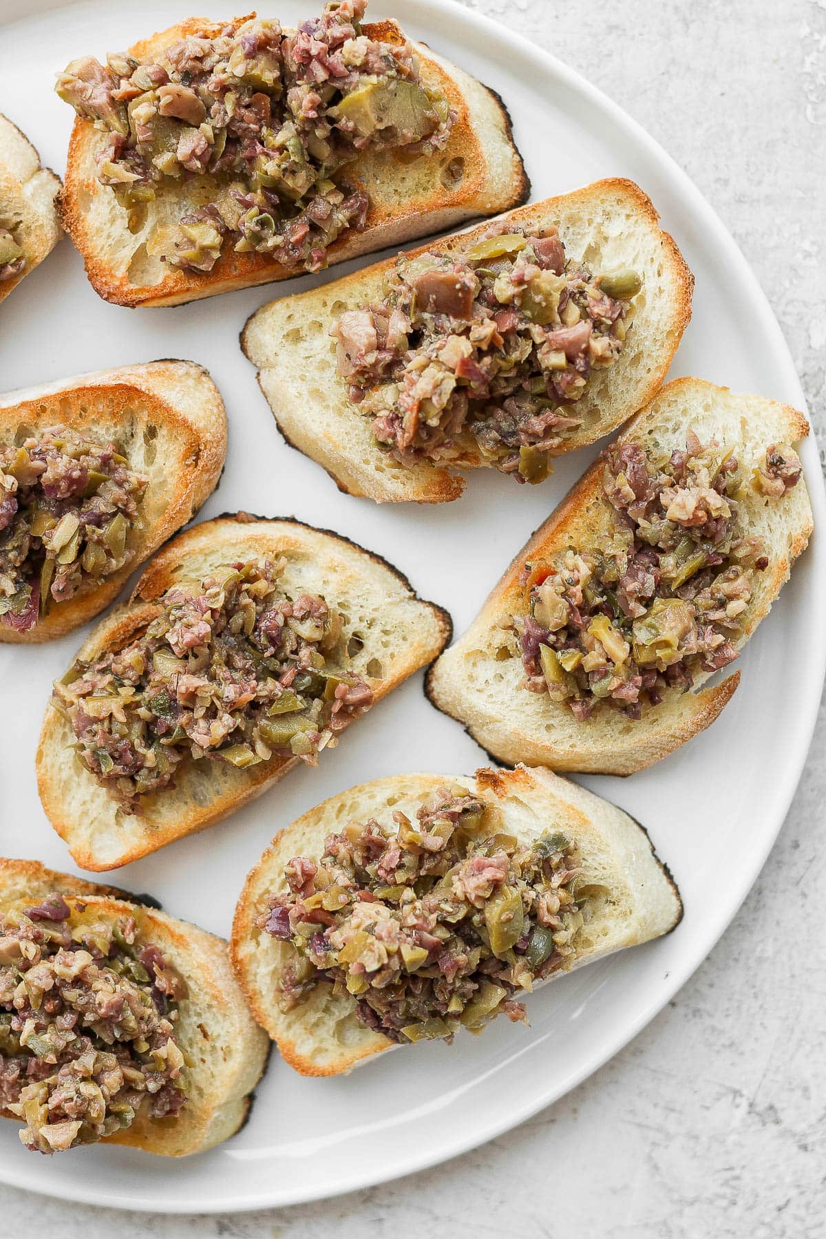 A plate of baguette slices with olive tapenade on top. 