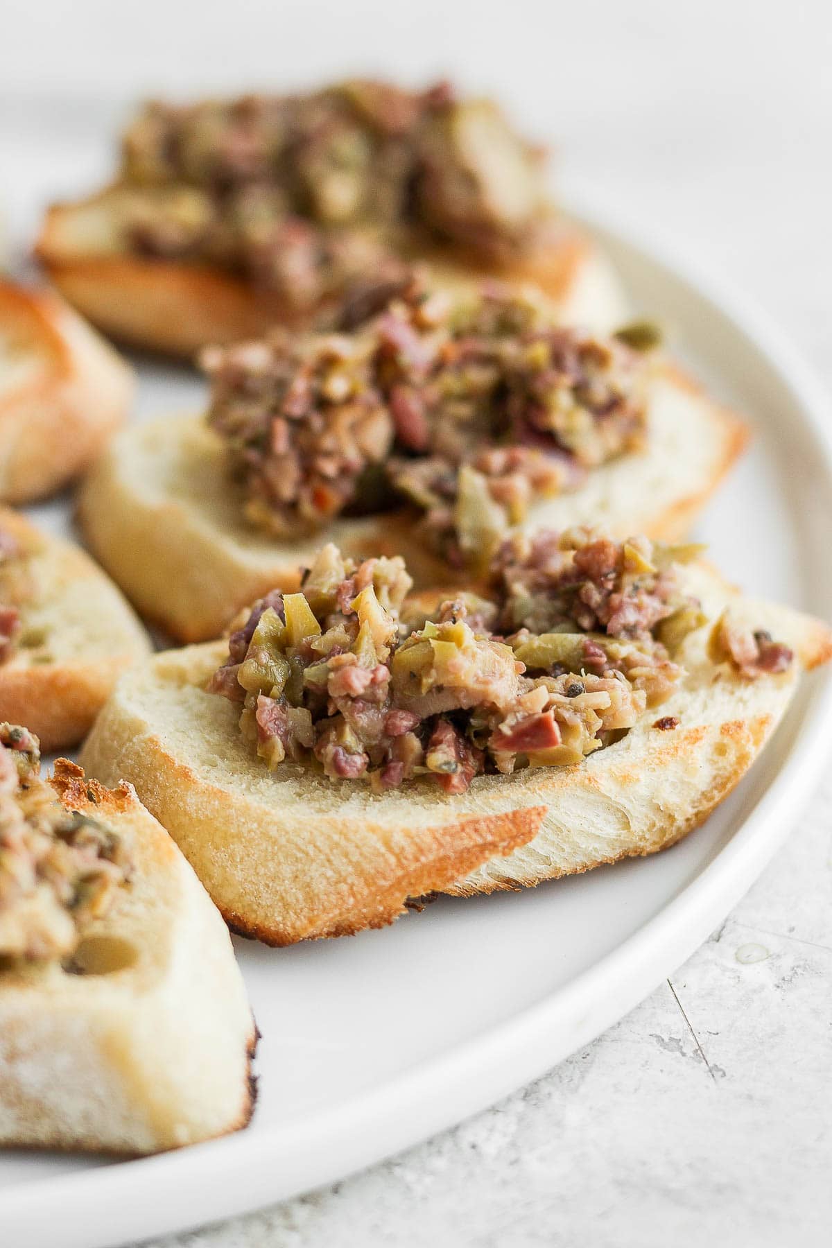Side shot of a plate of baguettes with olive tapenade on top. 