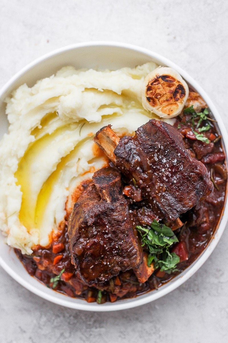 A bowl of mashed potatoes with braised short ribs on top.