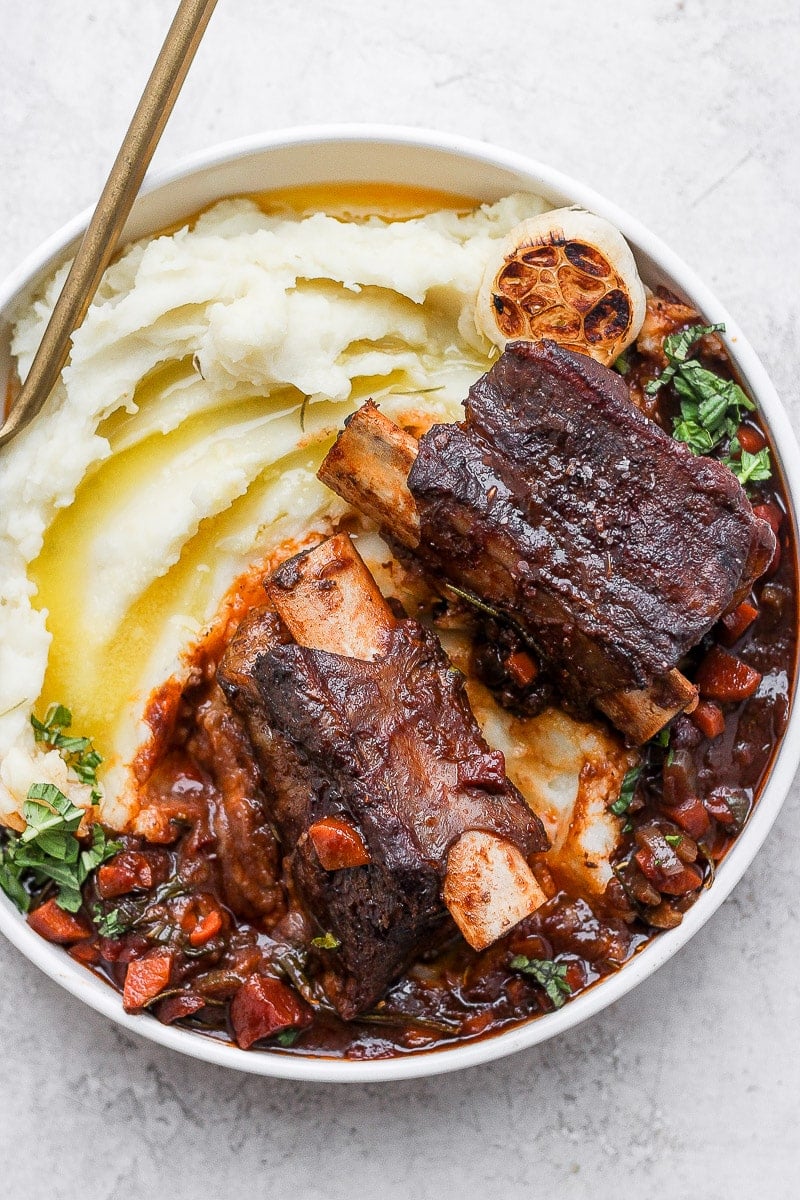 A bowl of mashed potatoes with braised short ribs on top.