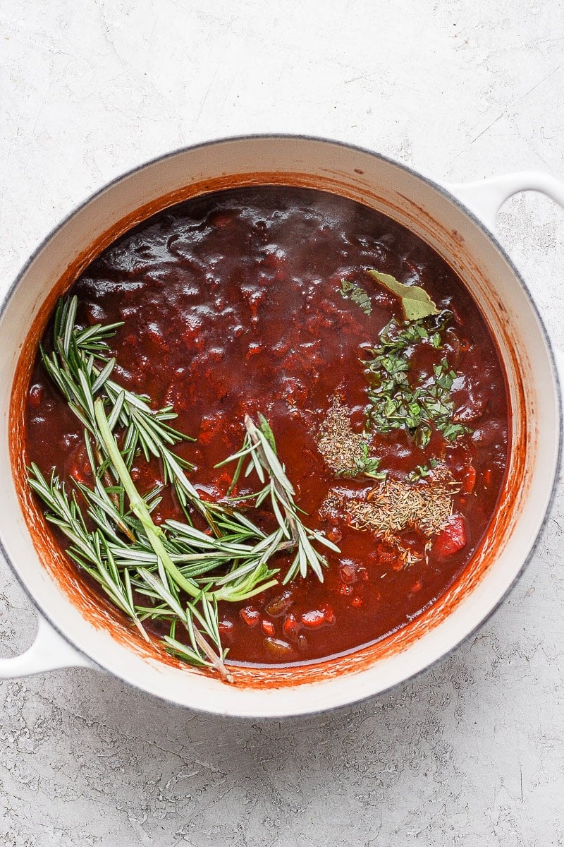 Braising liquid in a Dutch Oven with fresh herbs on top.