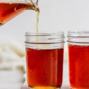 A glass pitcher pouring homemade maple syrup into a mason jar with another jar of syrup next to it.