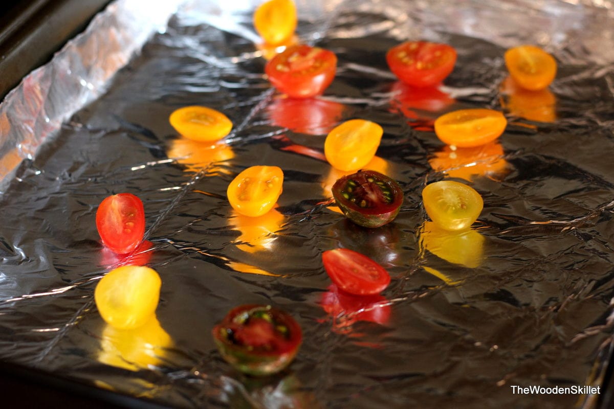 cherry tomatoes cooking on a foil-lined baking sheet. 