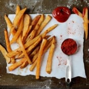 Baked french fries on a piece of parchment paper with some ketchup and a tablespoon of paprika.