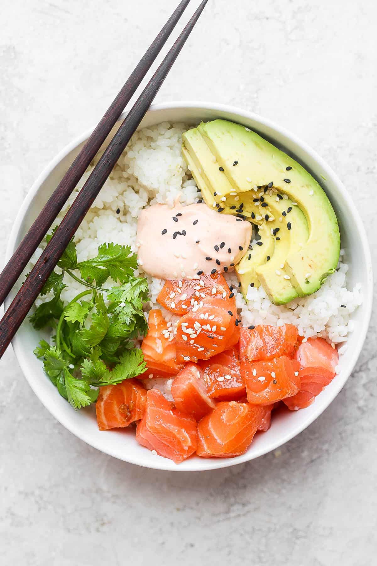 A salmon sushi bowl filled with rice, raw salmon, cilantro, avocado and spicy mayo. 