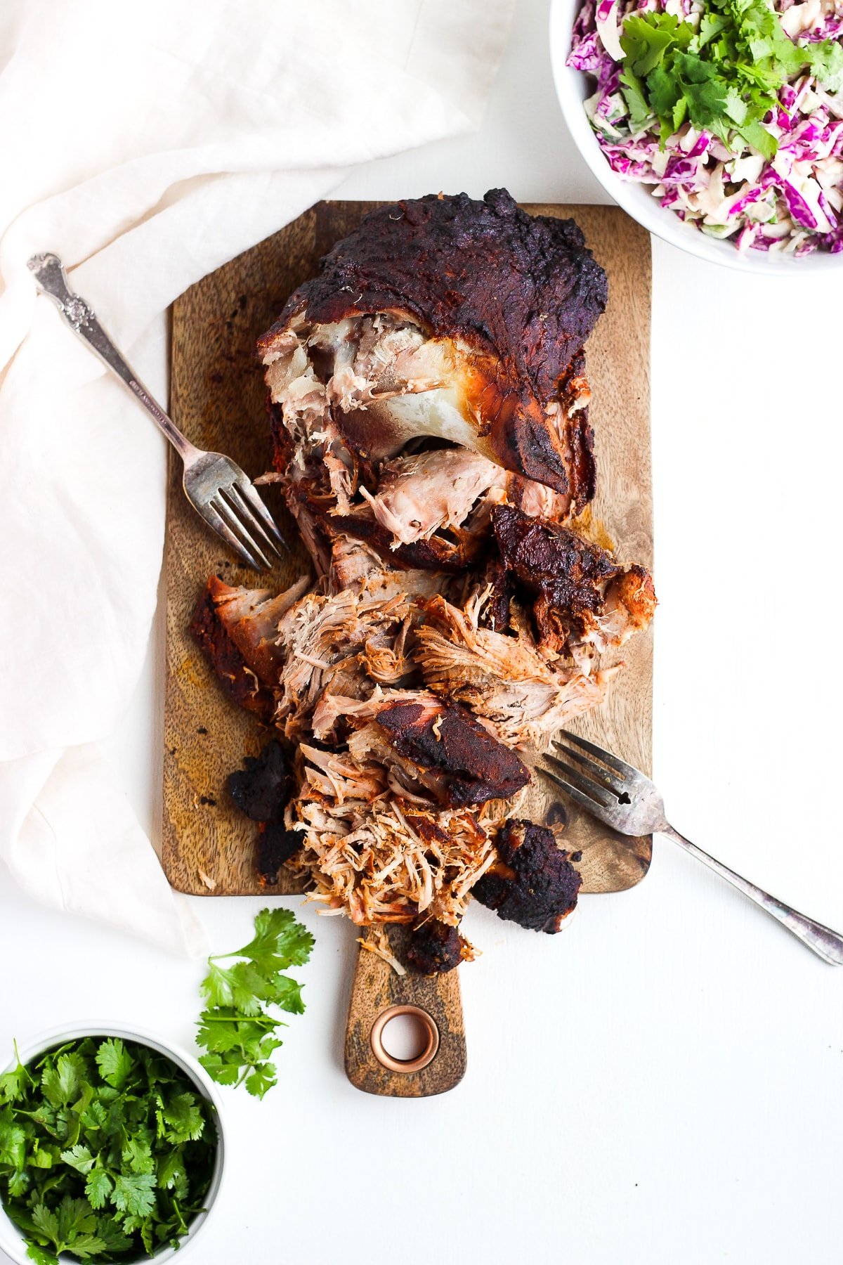 A smoked pork shoulder, partially shredded, sitting on a wooden board. 