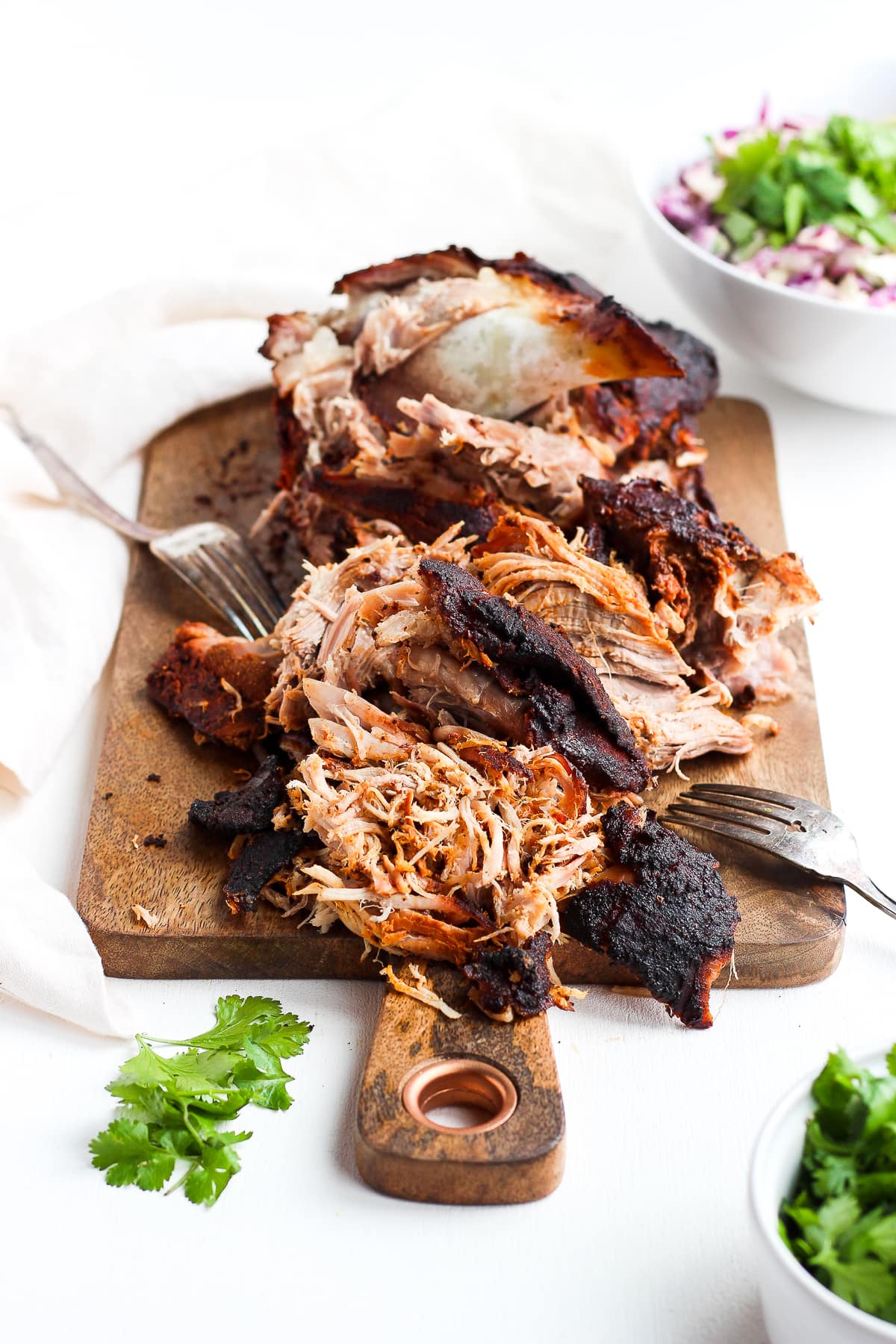 A smoked pork shoulder, partially shredded, sitting on a wooden board. 