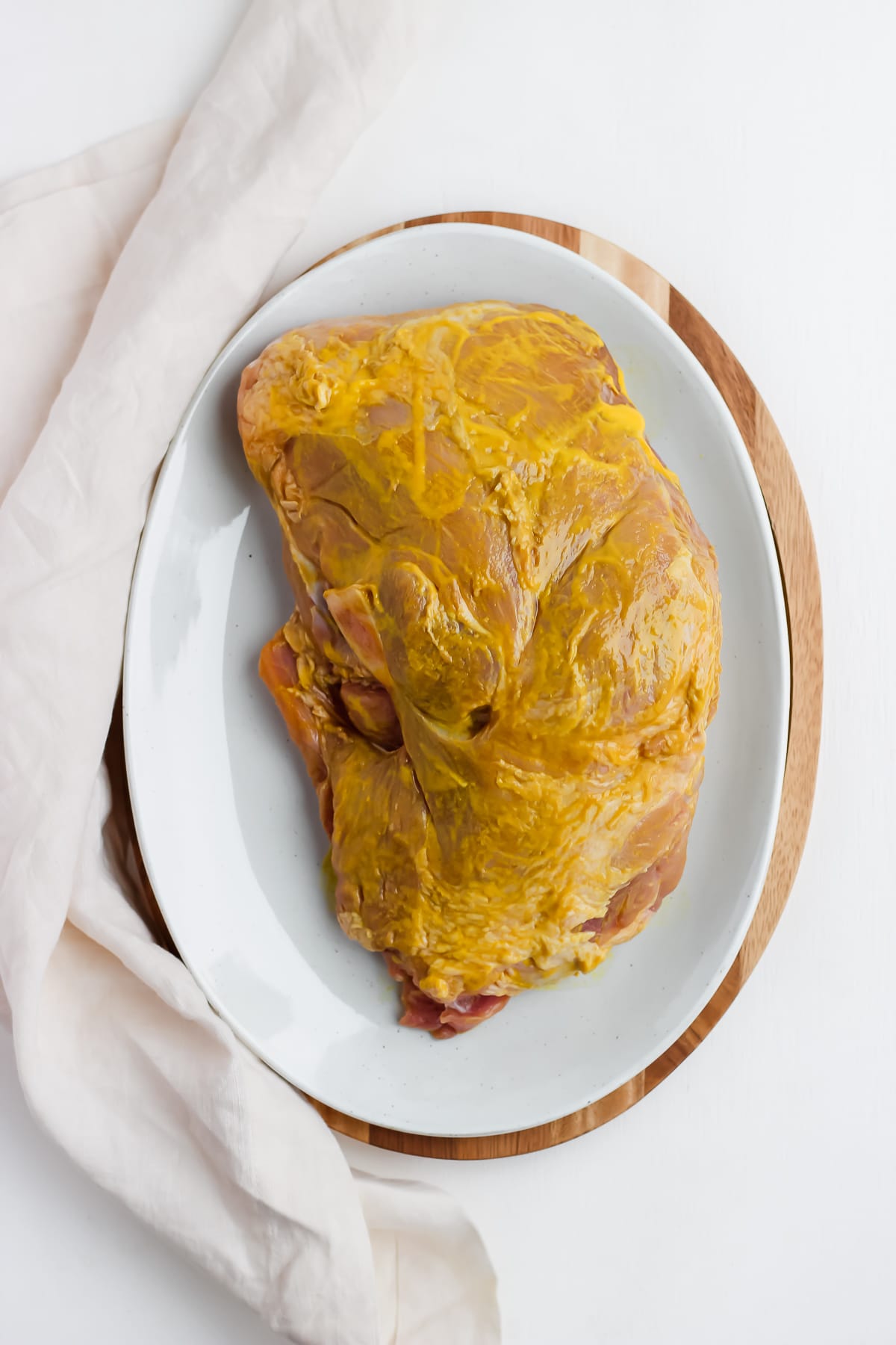 Pork shoulder on a large plate rubbed in yellow mustard. 