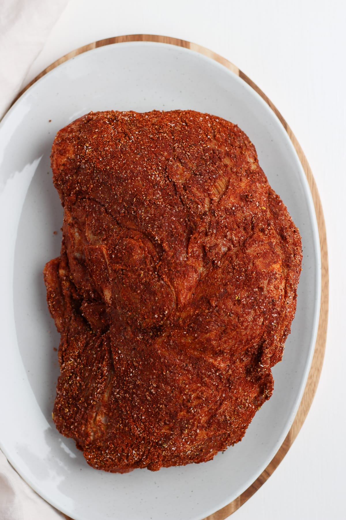 Pork shoulder sitting on a large platter with pork rub on it. 