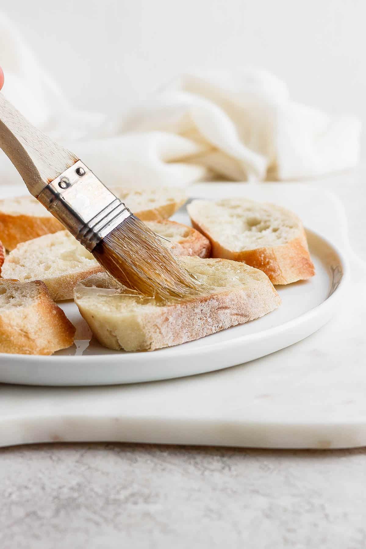 A basting brush that's brushing olive oil on a baguette slice.