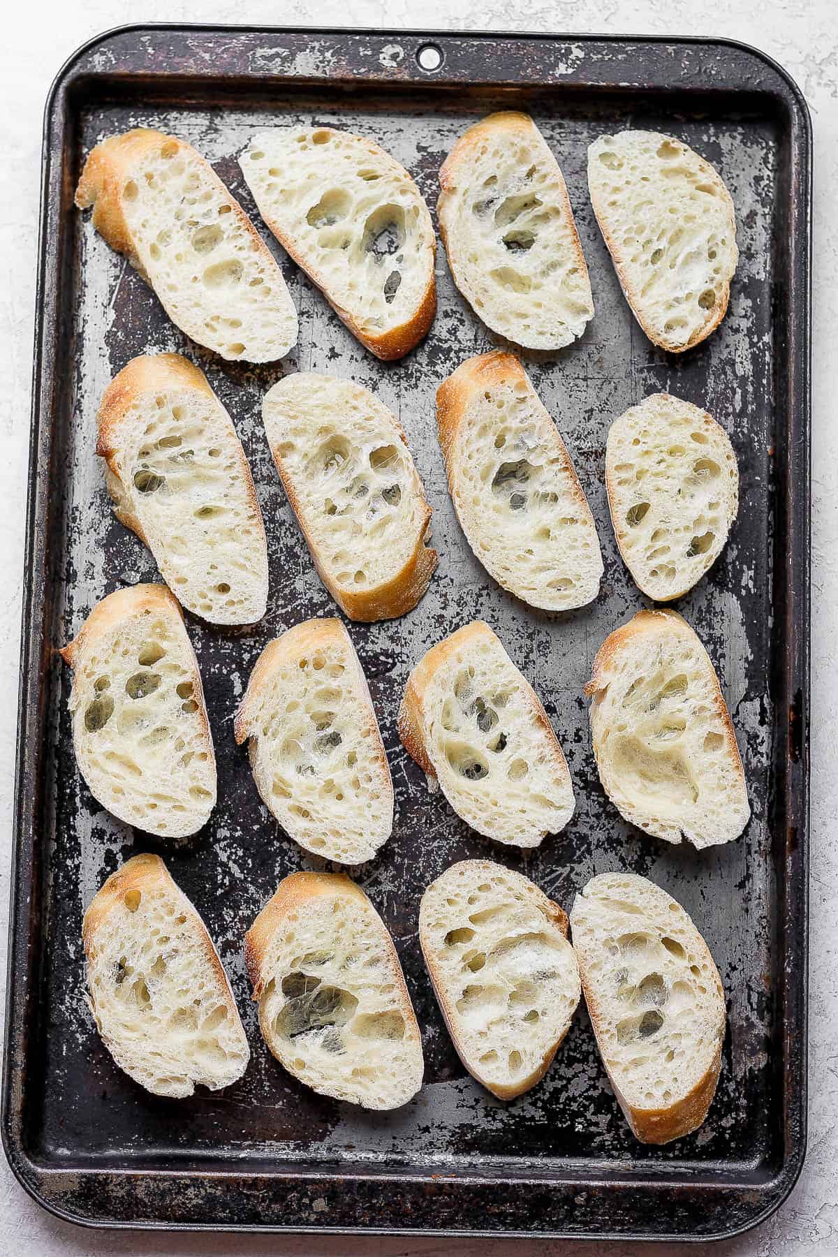 16 pieces of sliced baguette on a baking sheet.