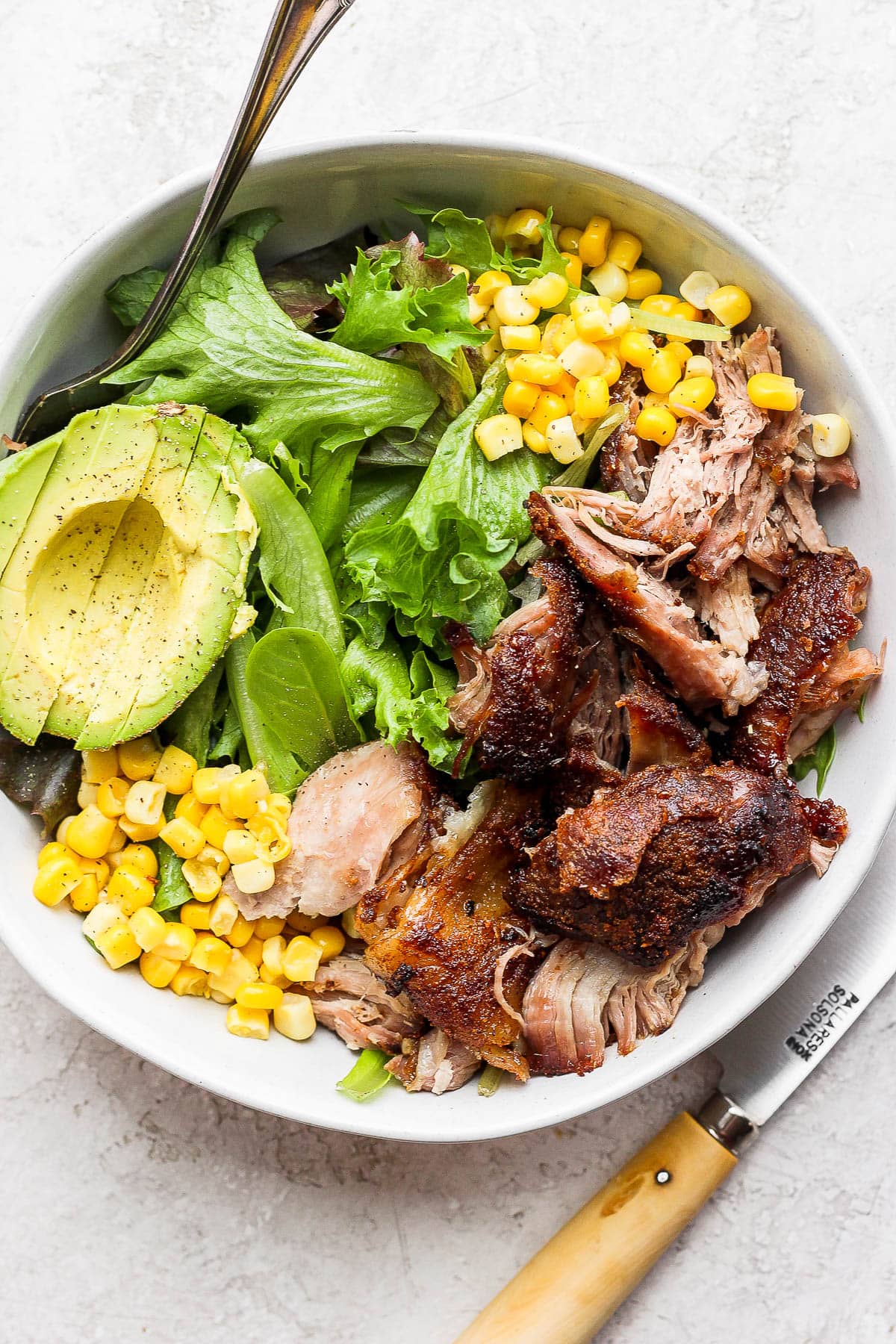 A pulled pork salad in a bowl with corn and avocado. 