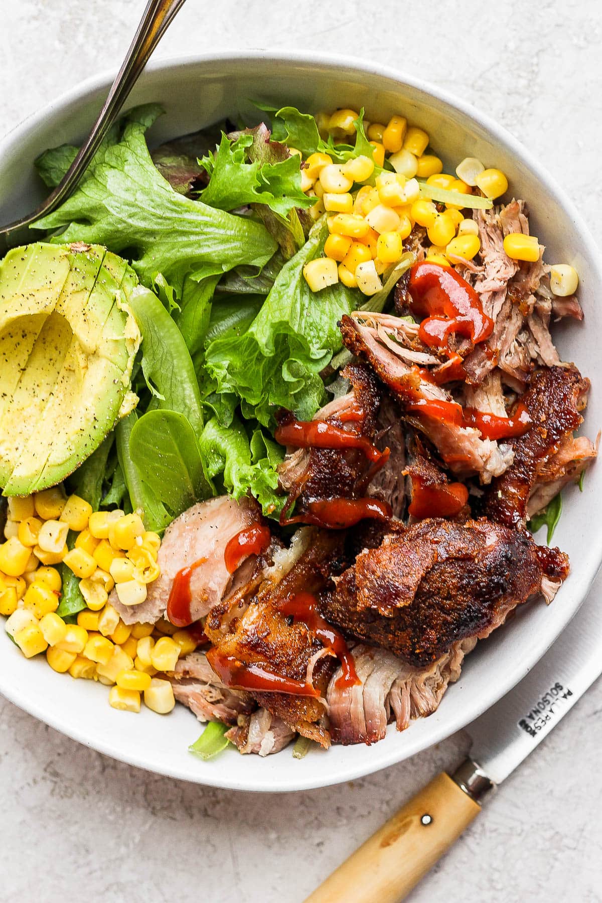 A pulled pork salad in a bowl with corn and avocado. 