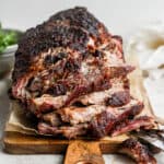A smoked pork shoulder on a wooden board, partially shredded.