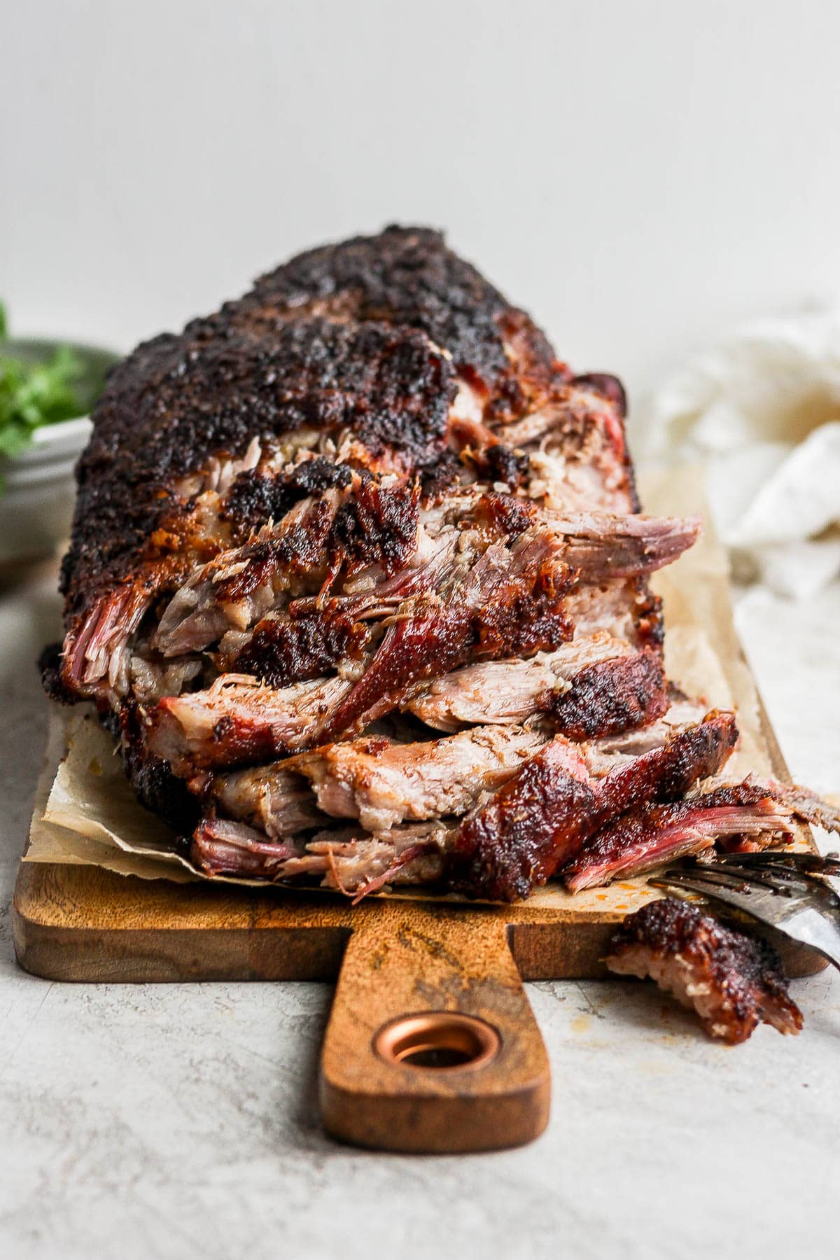 A smoked pork shoulder on a wooden board, partly shredded. 