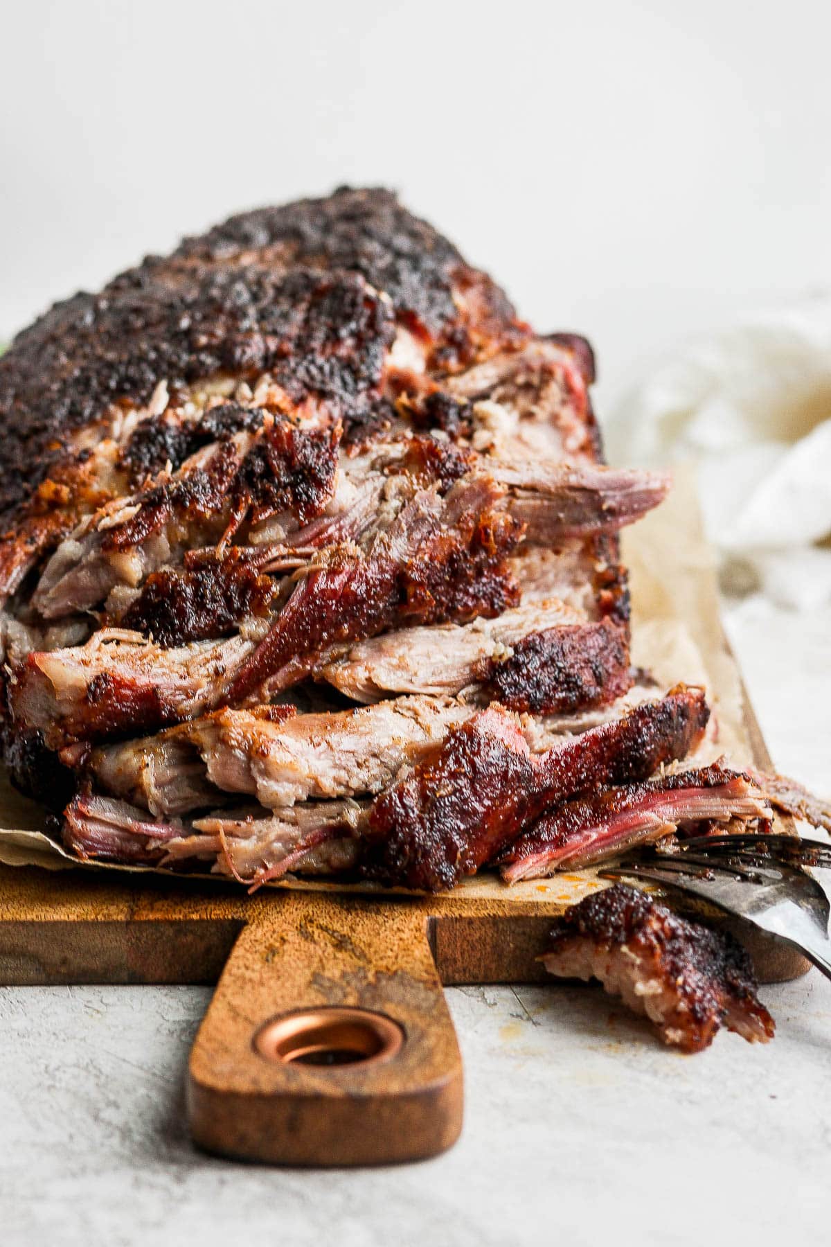 A smoked pork shoulder, partially shredded, sitting on a wooden board. 