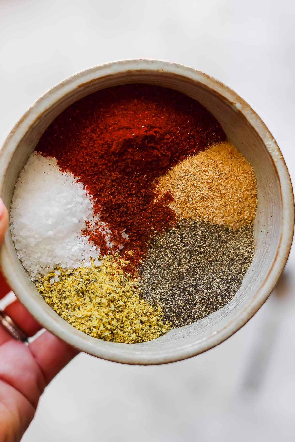 Someone holding a bowl of pork dry rub ingredients, unmixed.