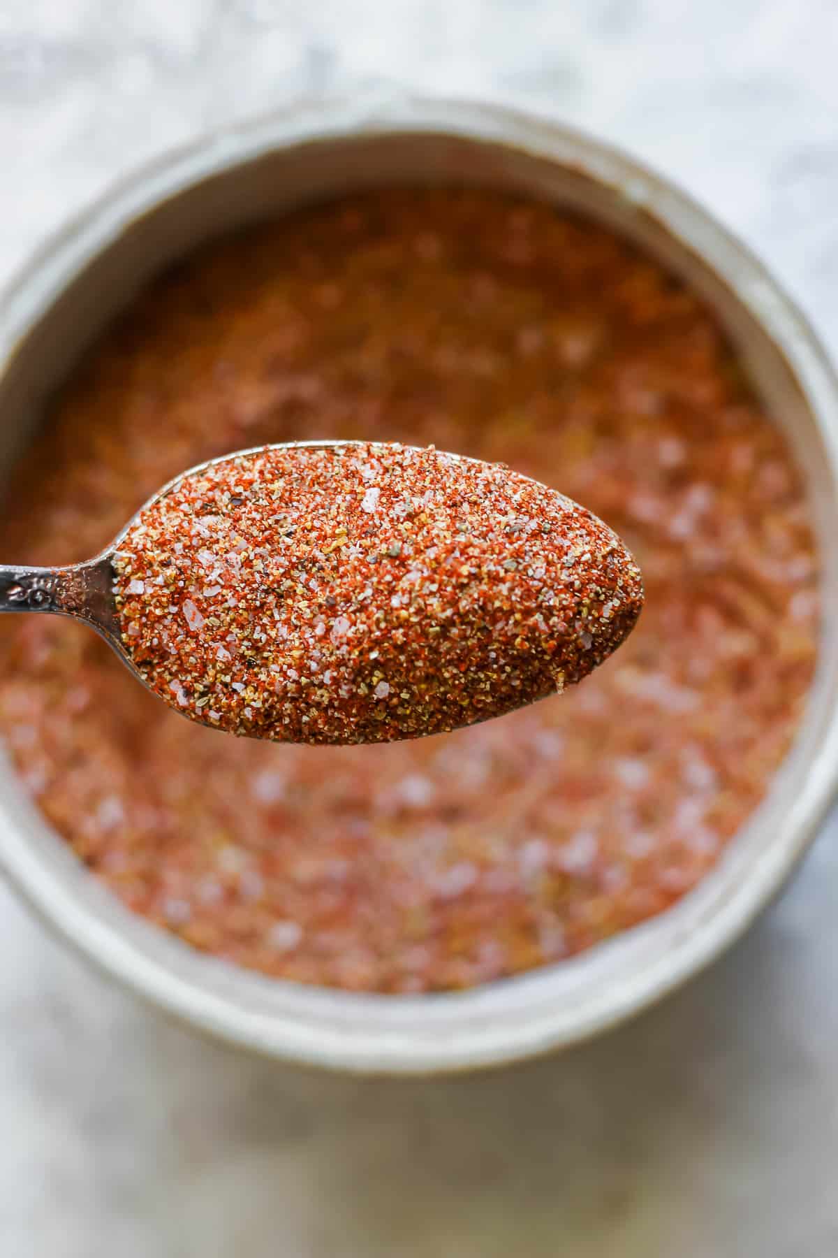 A bowl of mixed up dry rub ingredients with a spoon holding some over the bowl.