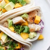 A white plate with three tilapia tacos next to each other.