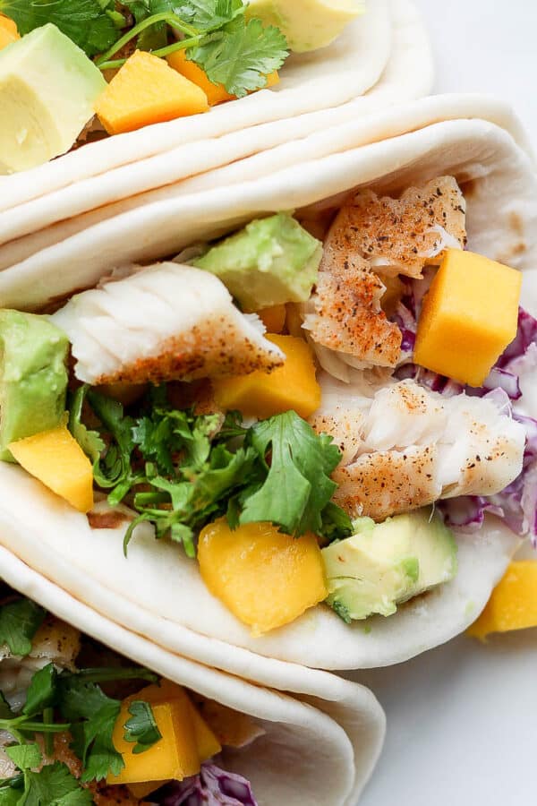 A white plate with three tilapia tacos next to each other.